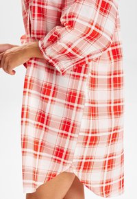 Robe chemise à carreaux rouges et blancs avec des manches longues, des boutons décoratifs et un ourlet arrondi. Fabriquée dans un tissu léger et texturé.