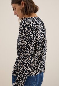 Pull à manches longues bleu marine avec un imprimé léopard beige. Fabriqué en tissu doux, avec une coupe décontractée et des détails à fentes sur les côtés.