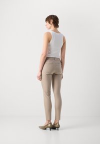 Hvit ermløs topp kombinert med tettsittende beige bukser og metallisk hæl-sko, sett fra bak, som fremhever det glatte stoffet og skreddersømmen.