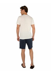 Maglietta bianca a maniche corte in misto cotone, con scollatura rotonda, abbinata a pantaloni corti blu navy. I pantaloni hanno una vestibilità rilassata e tasche posteriori.
