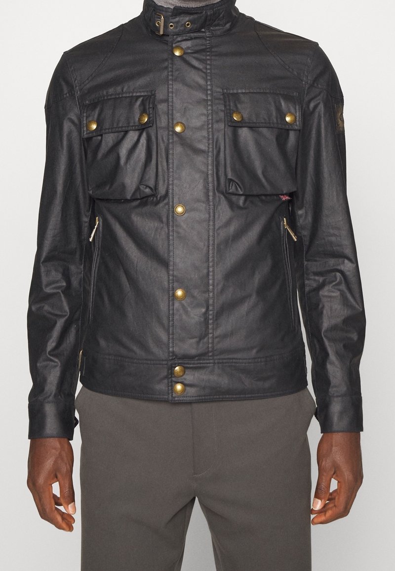 Svart läderjacka med en figurnära design, som har två stora bröstfickor, guldknapp och dragkedjedetaljer på sidorna.