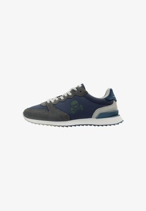 Zapatilla en azul marino y gris con cordones blancos, suela texturizada y logo de calavera y huesos cruzados en verde oscuro en el lateral.