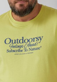 T-shirt en coton jaune clair avec un col rond, arborant un texte bleu foncé : "Sensations de plein air à venir ! Abonnez-vous à la nature."