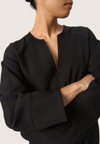 Svart ribbad topp med V-ringning, vida ärmar och framträdande sömnadsdetaljer. Tyget har en texturerad yta.