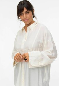 Camicia bianca con bottoni, dalla vestibilità rilassata, maniche lunghe e colletto, realizzata in tessuto leggero e leggermente stropicciato.