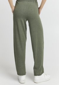 Lette, løstsiddende olivengrøn sweatpants med en blød tekstur og elastisk talje, parret med hvide sneakers.