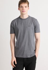 Γκρι βαμβακερό t-shirt με στρογγυλή λαιμόκοψη, κοντά μανίκια και ένα μικρό μαύρο λογότυπο τυπωμένο στο αριστερό στήθος. Θεμελιώδης, απλός σχεδιασμός.