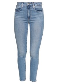 Jeans skinny de tiro alto azul claro con bolsillos delanteros y traseros, cierre de botón y textura descolorida en los muslos y las rodillas.