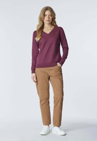 Maglione a V in tessuto borgogna, abbinato a pantaloni beige e sneakers bianche. Il maglione presenta maniche lunghe e un orlo a coste.