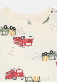 T-shirt di cotone color crema con illustrazioni di cartoni animati di camion dei pompieri rossi e veicoli verdi, con accenti di stelle giocose.