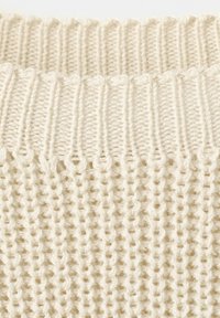 Primo piano di tessuto lavorato a maglia color crema che mostra texture a coste e a waffle.