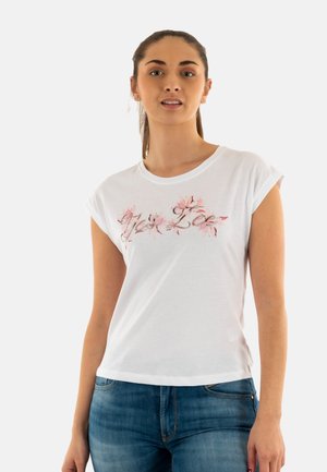 T-shirt bianco di cotone con maniche corte arrotolate e un design floreale nei toni del rosa. Abbinato a jeans in denim blu.