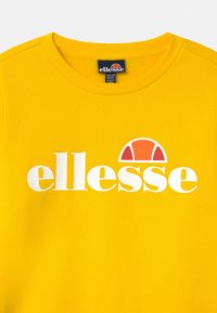 Žlutá mikina s kulatým výstřihem, žebrovaným límcem a bílým logem "ellesse" s oranžovým akcentem v designu. Hladká textura.