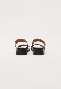 Sandalias de tacón negro con un acabado liso. Presentan dos correas delgadas que cruzan el pie y un tacón cuadrado. Suela interior marrón visible.