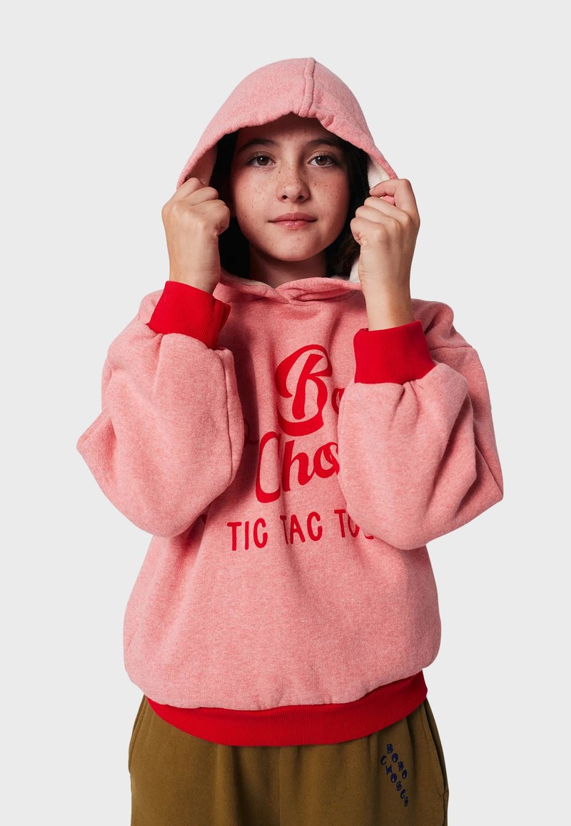 Sudadera rosa con acentos rojos y un logo en el frente. Presenta una capucha con cordones y puños acanalados. Tejido suave con un acabado texturizado.