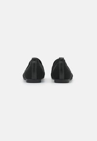 Zapatos negros con parte superior de malla, acentos de cuero, punta redondeada y suela plana. La vista trasera destaca los detalles de costura y las lengüetas en el talón.