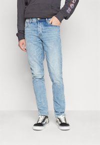 Light blue denim jeans with a slim fit, featuring a classic five-pocket design, subtle fading, and a metal button closure.