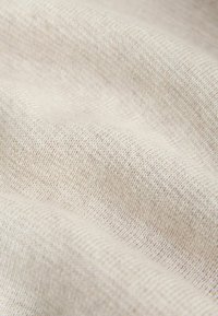 Tissu beige clair texturé avec un motif tissé fin. La surface semble douce, présentant des variations subtiles de ton et de texture.