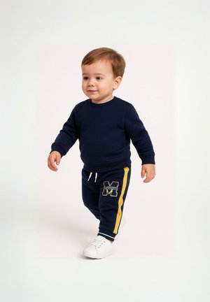 Granatowy sweatshirt i pasujące dresy z żółtymi bocznymi paskami. Spodnie mają naszywkę z logo "M". Białe sneakersy dopełniają outfit.