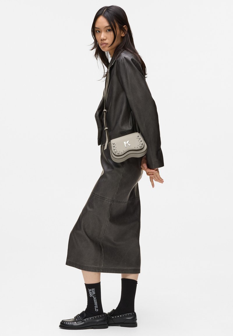 Giubbotto di pelle nera e gonna lunga abbinata, completati da una borsa grigia con borchie e un logo. Scarpe nere con dettagli decorativi.