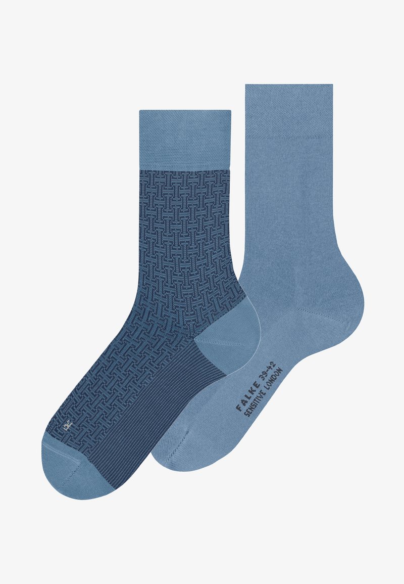 Ζευγάρι μπλε κάλτσες crew, η μία με γεωμετρικό σχέδιο και η άλλη μονόχρωμη μπλε με μαύρο κείμενο στη σόλα, τοποθετημένες δίπλα δίπλα.