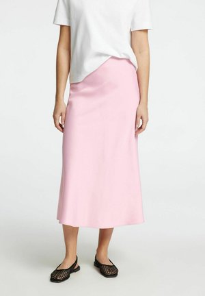 Lys pink midi nederdel lavet af glat stof, med en lige pasform. Kombination med sorte vævede slip-on sko. Hvid T-shirt delvist synlig.