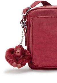 Borsa di stoffa rossa con accessori in argento lucido e un portachiavi con un grazioso ciondolo a forma di scimmia rossa pelosa, con un volto liscio e le braccia aperte.