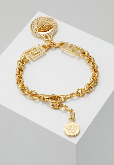 Gold chain bracelet featuring a medallion with a lion's head, set with rhinestones. Includes geometric link accents and a lobster clasp.