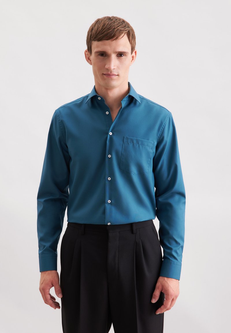 Teal langemouwen shirt met een klassieke kraag, voorkeurszak en witte knopen, gecombineerd met zwarte geplooide broeken. Soepele stofstructuur.
