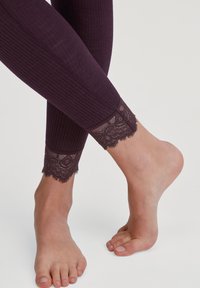 Leggings violets à côtes avec une délicate bordure en dentelle au niveau de la cheville. La texture douce et le design ajusté mettent en avant le motif en dentelle détaillé.