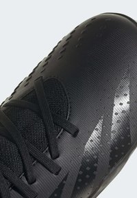 Svart fotbollssko med övre i strukturerad syntet, utrustad med snörning och subtila reflekterande detaljer i en smidig design.