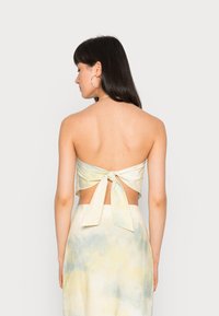 Top cropped com decote halter em um suave padrão tie-dye com tons de azul e amarelo, apresentando um design com nó nas costas e detalhe de costas abertas.