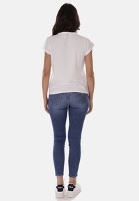 T-shirt bianca a maniche corte abbinata a jeans skinny blu. Il modello indossa sneaker bianche con dettagli neri. Completo semplice e casual.