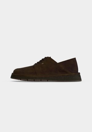 Dark brown suede men's lace-up shoe with thick rubber sole, viewed from the side on a plain light gray background.