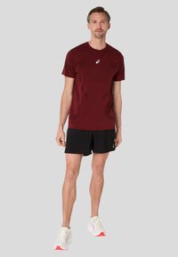 Bordeaux trænings t-shirt med korte ærmer, med struktureret detaljering. Sammen med sorte shorts og hvide sneakers med pink accenter.
