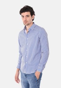 Camicia button-up con righe verticali blu e bianche, maniche lunghe e colletto a punta; realizzata in tessuto di cotone leggero.