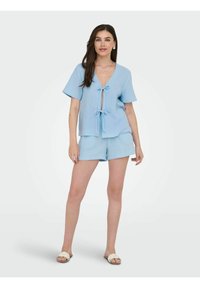 Maglietta corta in cotone azzurro chiaro con legatura frontale e scollo a V, abbinata a pantaloni corti coordinati. Design semplice con una finitura testurizzata.