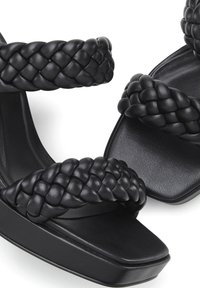 Zwarte haksandalen met gevlochten bands en een chunky plateauzool. Het materiaal lijkt glad met een matte afwerking.