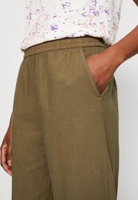 Un pantalon large vert olive présente une taille élastique, des poches latérales et un tissu doux et léger avec une texture lisse.