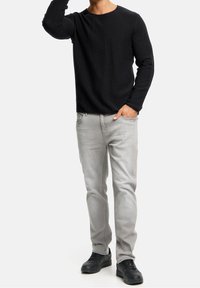 Zwarte, gestructureerde, lange mouwen shirt gecombineerd met lichtgrijze jeans en zwarte sneakers. Het shirt heeft een ronde halslijn en nauwsluitende mouwen.