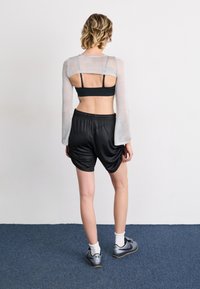 Black mesh shorts and a sheer, long-sleeve top with an open back. The outfit features a fitted black sports bra underneath.