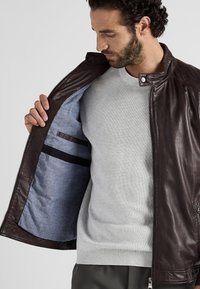 Brun läderjacka med dragkedja, med en strukturerad yta och ett blått tygfoder. Ficka inuti med horisontell randdetalj.