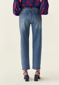 Jeans de denim azul claro, de corte recto, con dos bolsillos traseros y un ligero desgaste. Combinados con sandalias de tacón bloque negro.