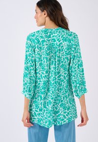 Groene en witte bloemetjesblouse met driekwart mouwen, een losse pasvorm en een plooidetail aan de achterkant. Lichtgewicht stof met een zachte textuur.