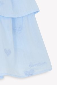 Lyseblå stoffkjole med lagdelt design, som har broderte hjerter og ordet "kjærlighet" i blå tråd nær kanten.