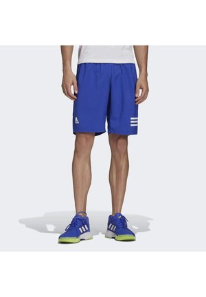 Man wearing blue Adidas athletic shorts and matching blue running shoes with white stripes, standing on a light background.