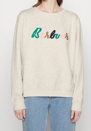 Béžová mikina s dlouhým rukávem s vícebarevným logem "Barbour" přes hrudník, nošená s světle modrými džínami.