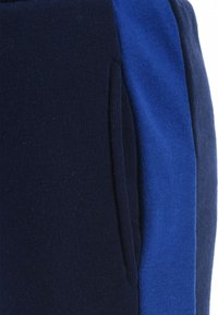 Marineblauwe en blauwe katoenmengsel trainingsbroek met een zijzak, met een gladde textuur en contrasterende kleurpanelen.