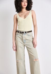 Light green ribbed tank top with a V-neck and wide straps paired with high-waisted light blue jeans featuring distressed knee rips and a brown belt.