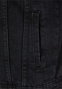 Zwart denimjack sectie die een zak toont met een strak ontwerp en subtiele textuur, gekenmerkt door een lichte glans en nette stiksels.